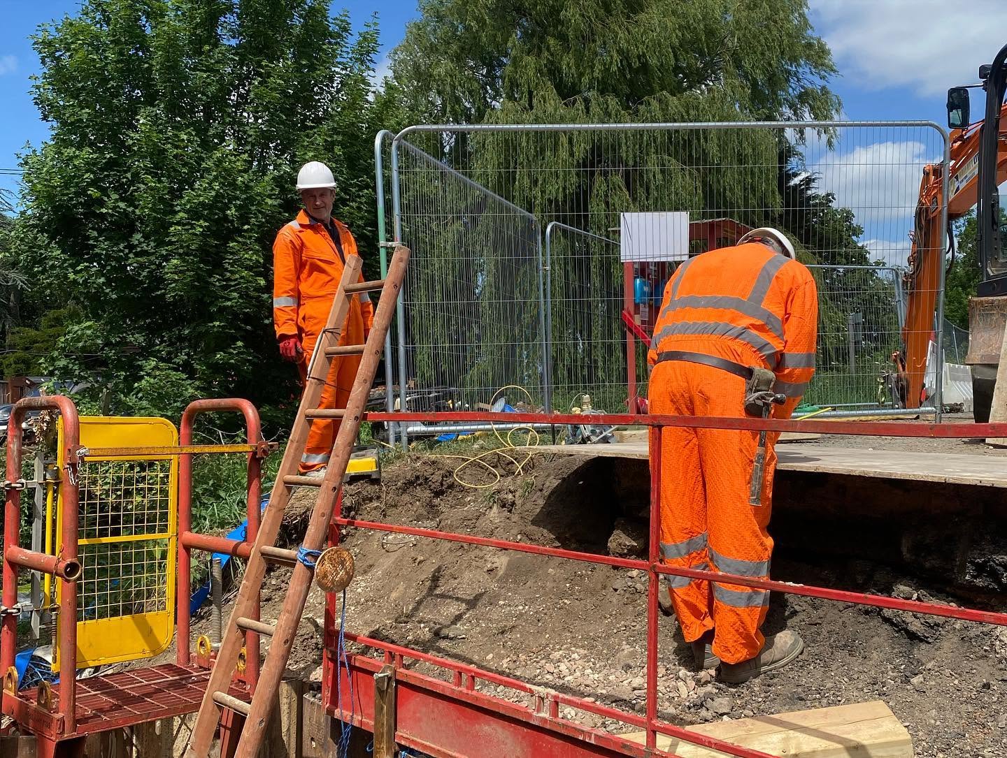 Two workers in high-visibility clothing on a culvert headwall site